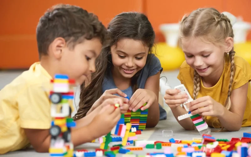 Happy kids playing with constructor at kindergarten. Children playing with colorful plastic bricks on the floor. Preschool kids having fun.