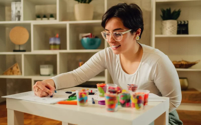 Smiling babysitter or nanny sitting on a floor with little kid while playing with clay. Mother help teach child boy colors and how to mold different shapes. Children development.